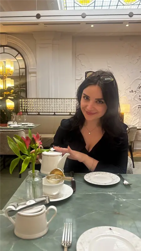 Ines seated at a table with a teapot, cups, and flowers